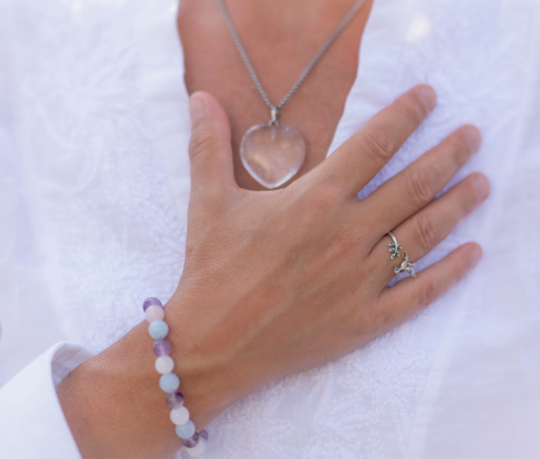 Frau legt Hand auf ihr Herz, trägt eine Kette mit einem Herzanhänger, einen Ring und ein buntes Armband.