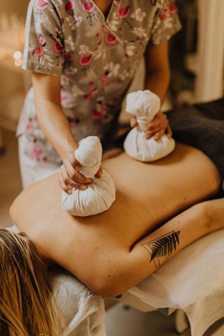 Eine Person erhält eine Massage mit heißen Kräuterbeuteln auf dem Rücken.