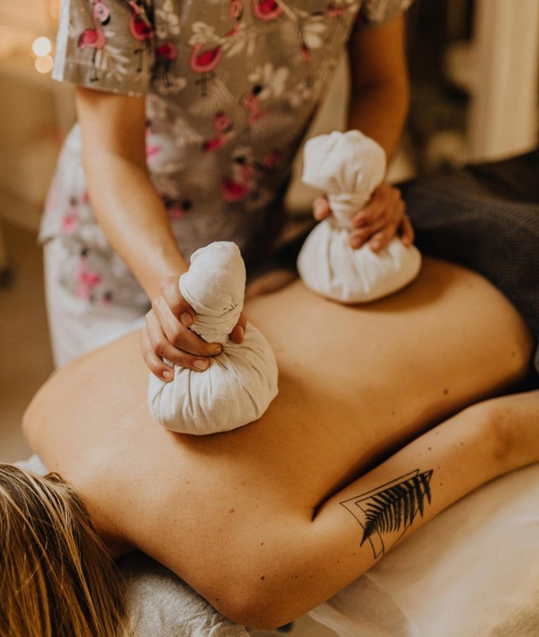 Eine Person erhält eine Massage für den Rücken mit Kräuterstempeln.