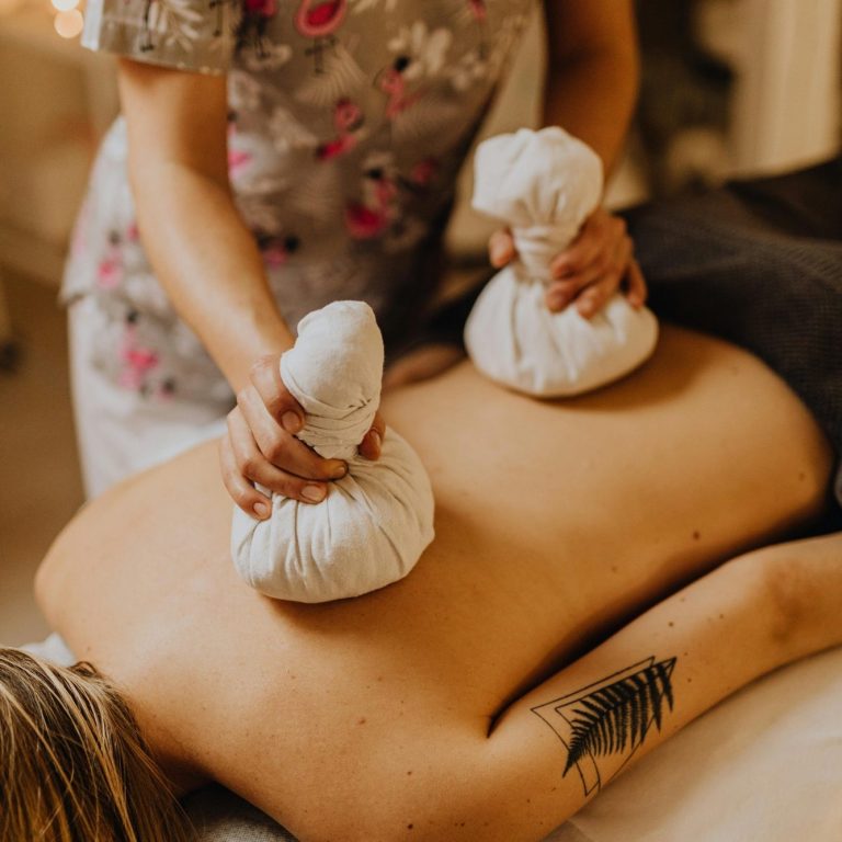 Eine Person erhält eine Rückenmassage mit heißen Kräuterkompressen.