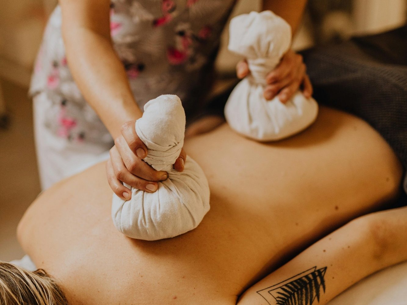 Eine Massage mit warmen Kräuterkissen auf dem Rücken einer liegenden Person.
