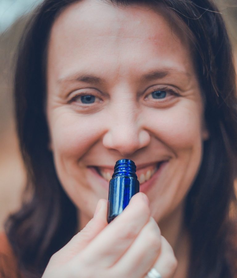 Frau lächelt und hält eine blaue Flasche ätherisches Öl nah an ihr Gesicht und Nase.