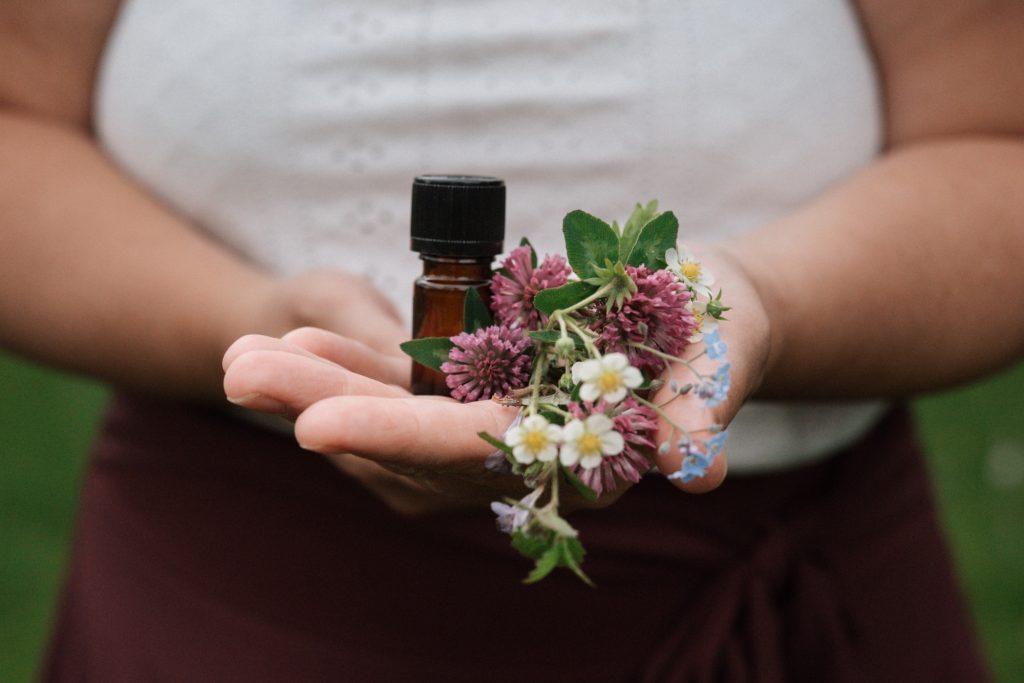 Eine Hand hält eine kleine Flasche und buntes Pflanzenmaterial.