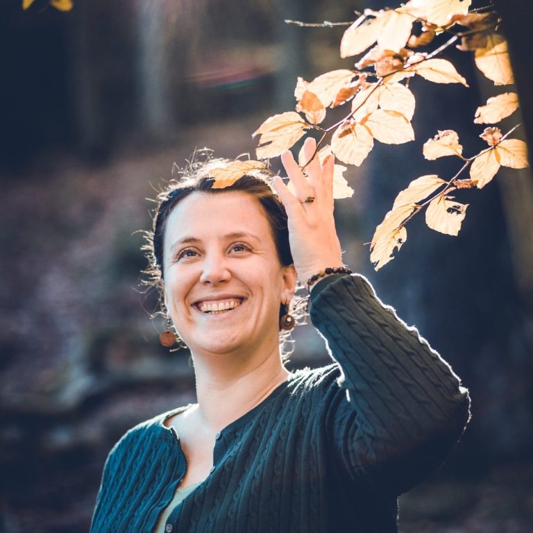 Frau mit lächelndem Gesicht, die einen Zweig mit gelben Blättern hält.