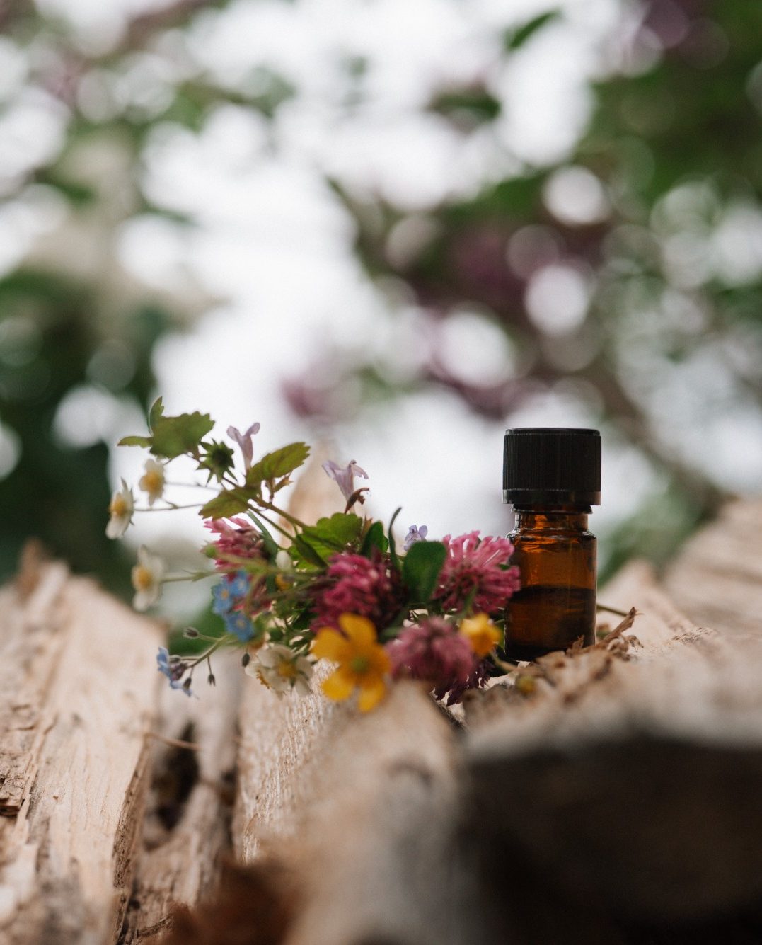 Braune Glasflasche mit bunten Blumen auf einem Holzstamm platziert.